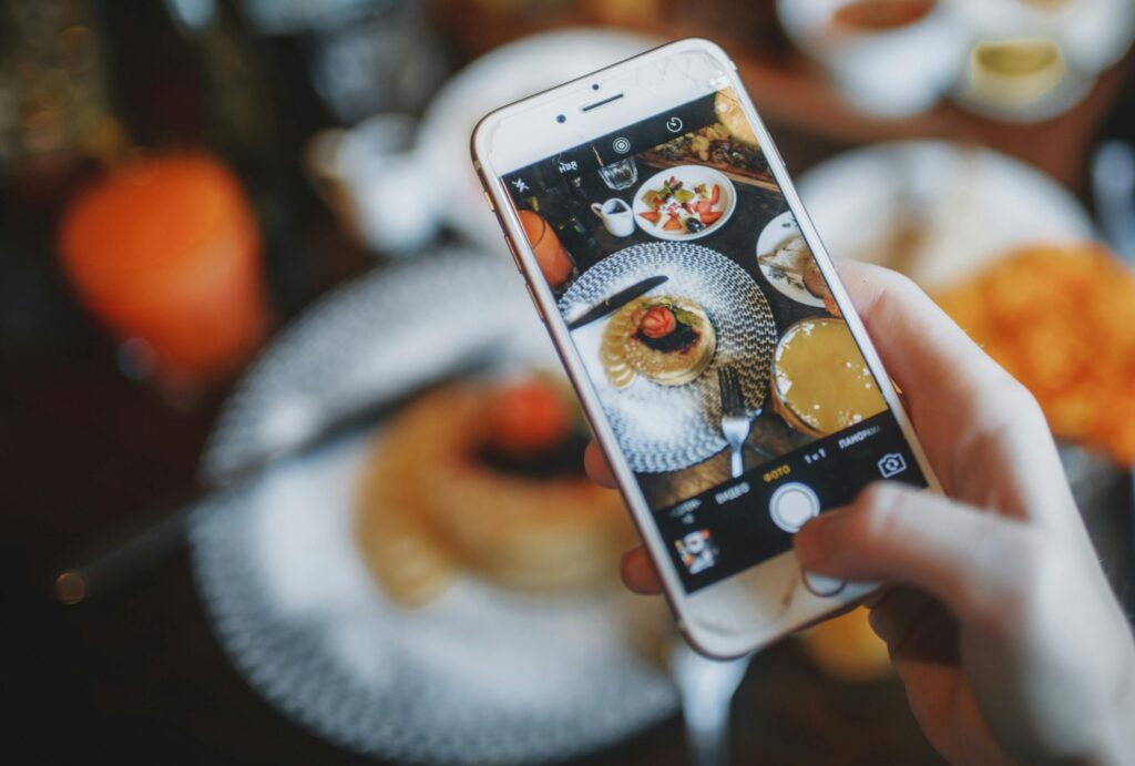Hand taking a photo of a delicious breakfast spread using a smartphone in a café setting.